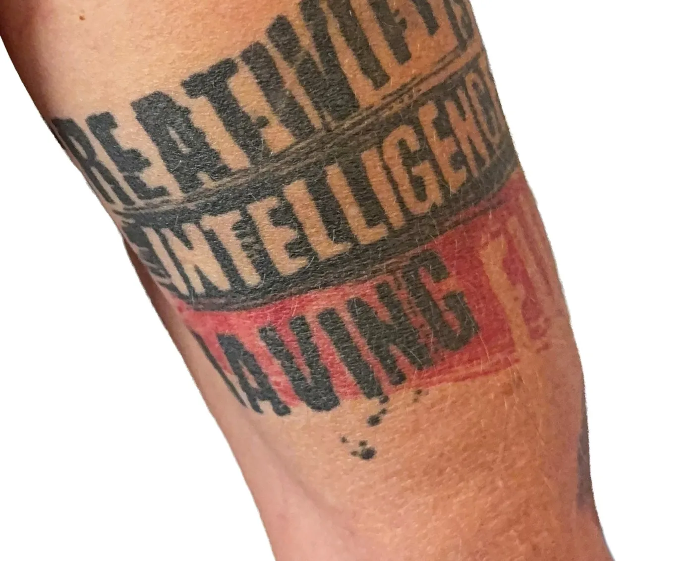 Jason's upper arm, tattooed with the words Creativity is Intelligence Having Fun in heavy black block letters, with Having Fun on a red band.
